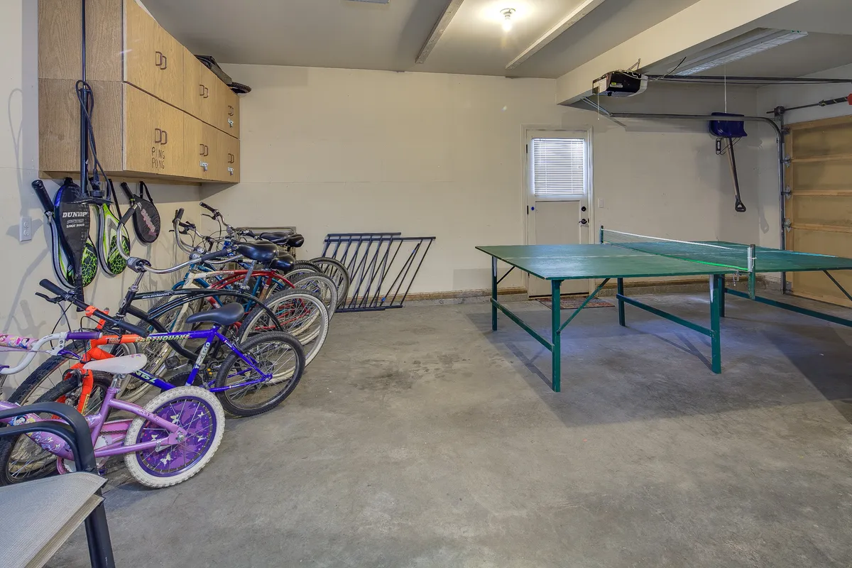 A playful and practical garage scene featuring bicycles, a ping pong table, and organized storage cabinets. The image highlights recreational amenities available on-site, including equipment for friendly ping pong matches and exploring the outdoors by bike.