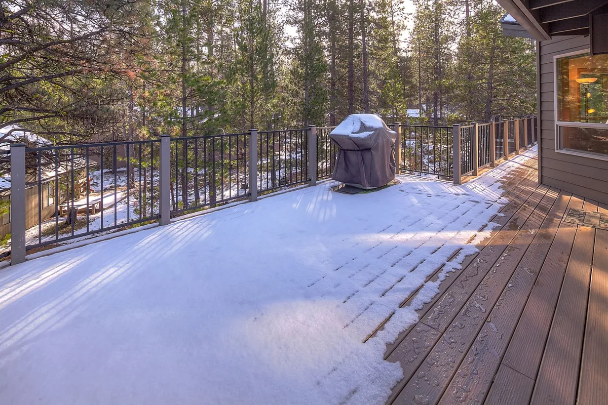 An exterior view of a deck featuring a grill, with the deck’s surface dusted in snow and trees visible in the background. The setup underscores the deck’s function as a year-round spot for barbecuing, gathering, and enjoying the natural surroundings in any season.