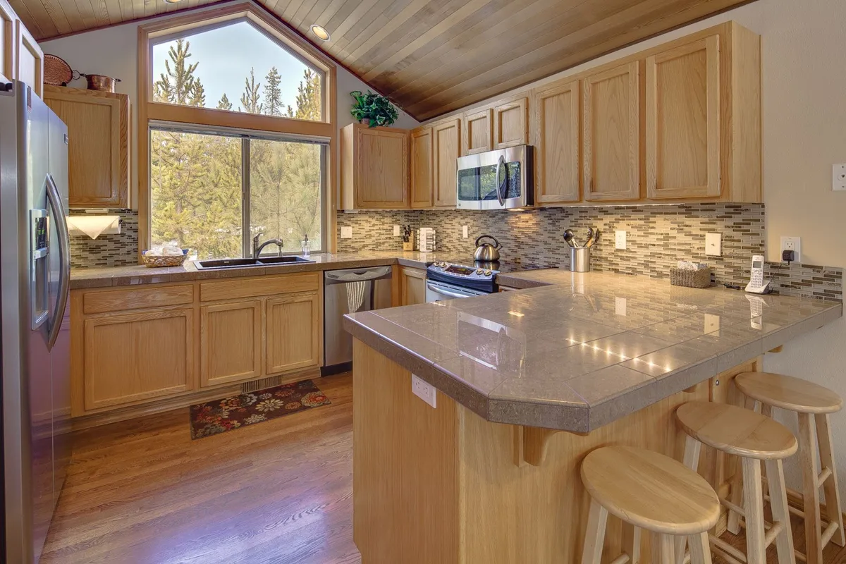 A bright, functional kitchen with a central island, large window, stainless steel appliances, and wooden cabinetry. Sunlight streams in, illuminating the space where families can cook, entertain, and make lasting memories together.
