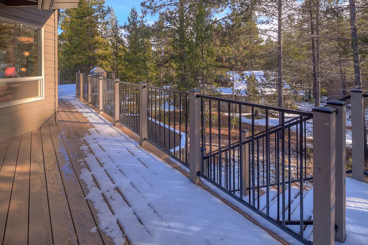 A serene exterior deck is surrounded by tall trees and a snow-covered yard. The deck is an inviting spot to relax, watch wildlife, or stargaze after a day of activities, with nature just beyond the railing.