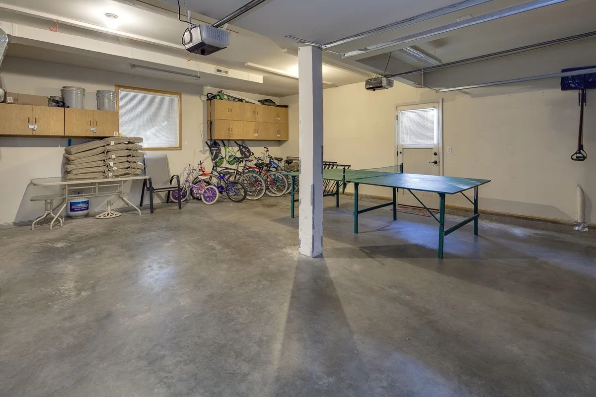 An organized garage or activity room featuring a table tennis table, storage cabinets, and bicycles. The setup is practical, inviting friendly competition and suggesting readiness for group activities both indoors and out.