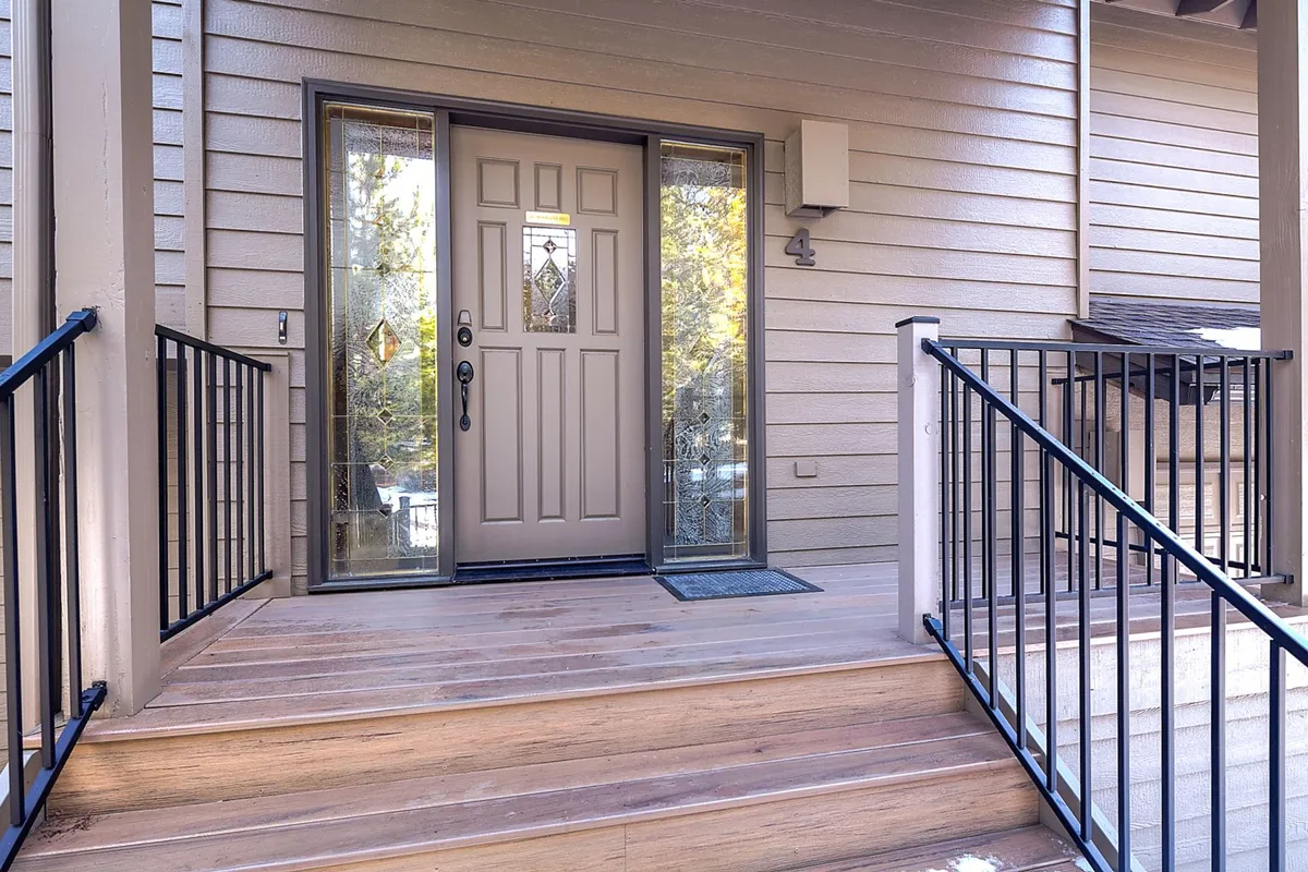 A welcoming exterior view of the front door, staircase, and porch railings. The inviting entrance, set against a backdrop of trees, hints at both arrival and outdoor connection.