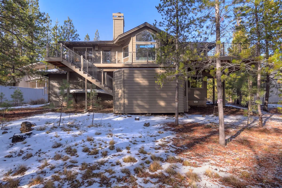 This exterior image showcases a spacious wooden deck bordered by large windows and surrounded by lush trees. The deck is visibly suited for gatherings, with ample space for seating and outdoor activities. The natural setting and inviting design signal opportunities for relaxation, dining, and socializing in the open air.