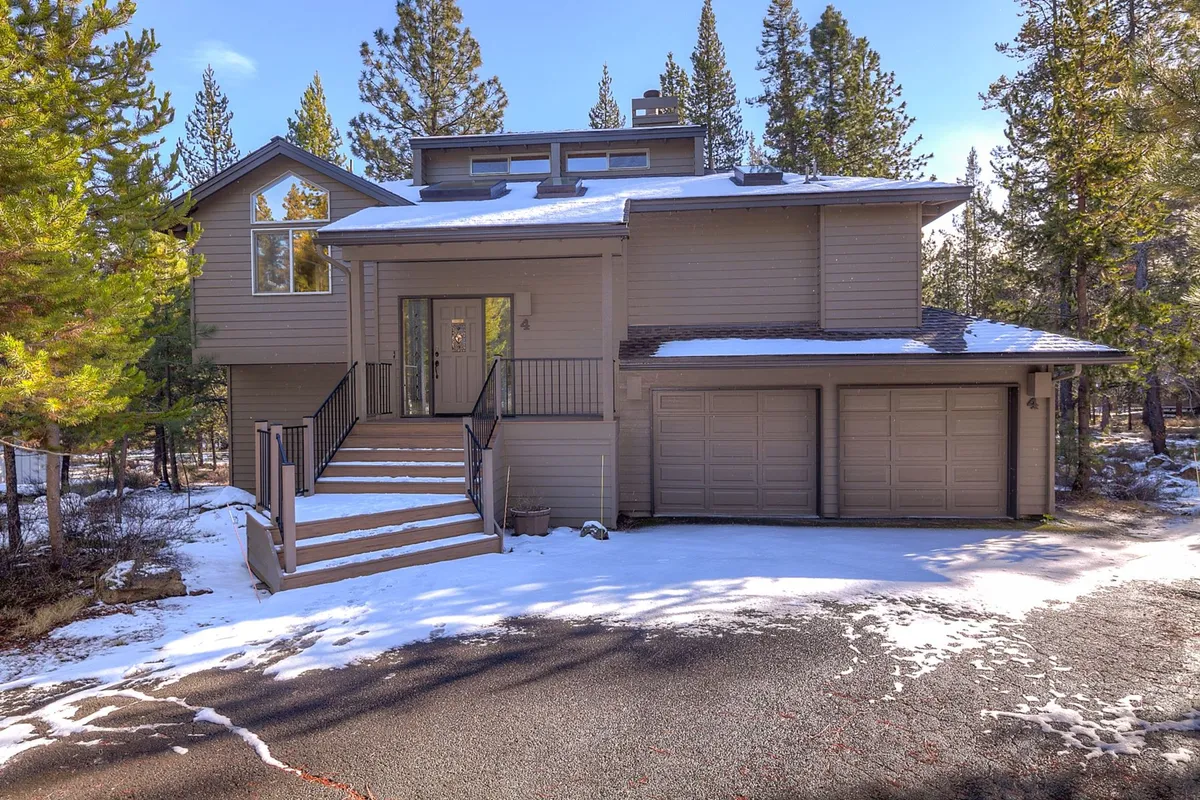 This exterior image shows the home's front entrance surrounded by trees, with the garage doors visible and a snow-dusted landscape, evoking a sense of arrival and connection to the outdoors. The scene suggests easy access to nearby parks and trails, as well as the welcoming home base for family adventures.