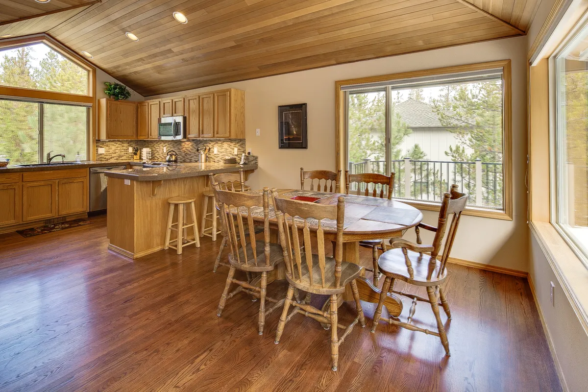 An open dining area connected seamlessly to a modern kitchen, featuring a dining table and kitchen counter backdropped by expansive windows that let in plenty of daylight. The setting inspires thoughts of shared meals, celebrations, and casual brunches, all in a space bathed in warmth and light.