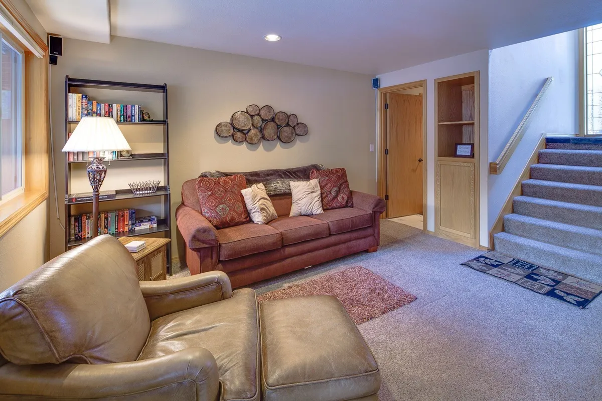 This image features a cozy living area with a sofa, bookshelf, stairs, and a rug. The space is inviting and flexible, suitable for movie nights, reading, or relaxed socializing, and its proximity to stairs hints at the split-level layout.
